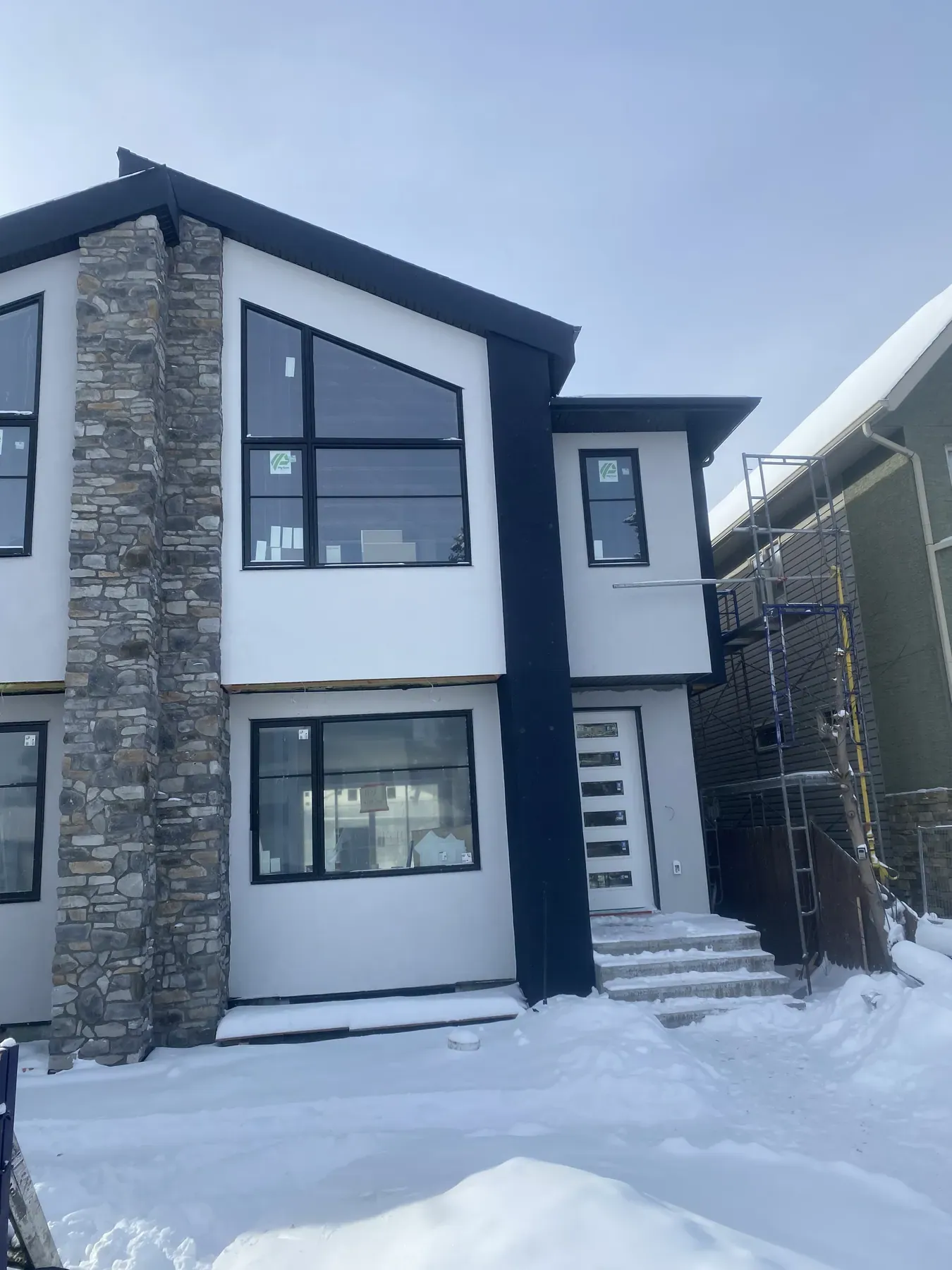Two-storey infill duplex in Calgary with white acrylic stucco, a natural stone column and black window frames