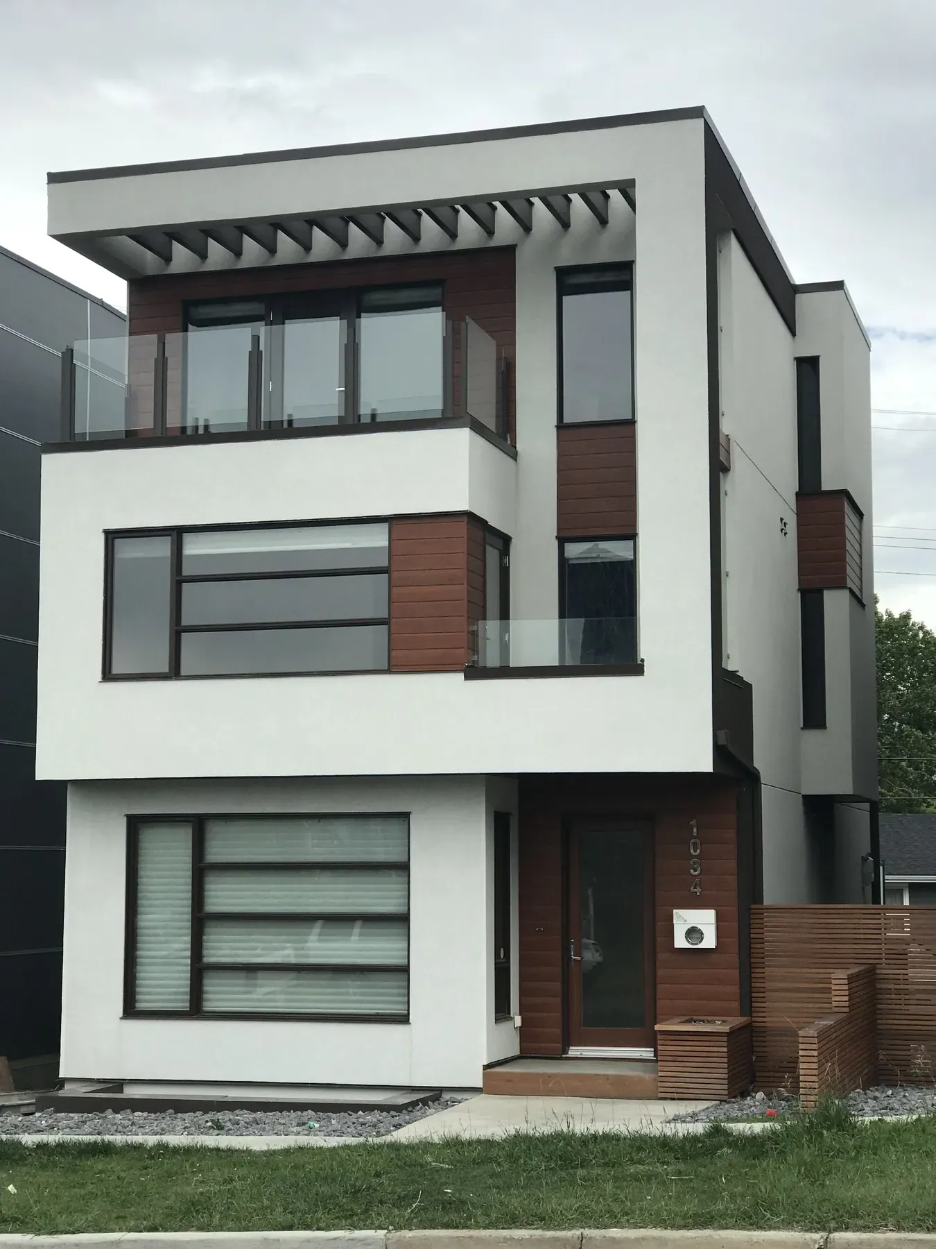 White three-storey modern infill home with acrylic stucco, cedar accents and black window frames